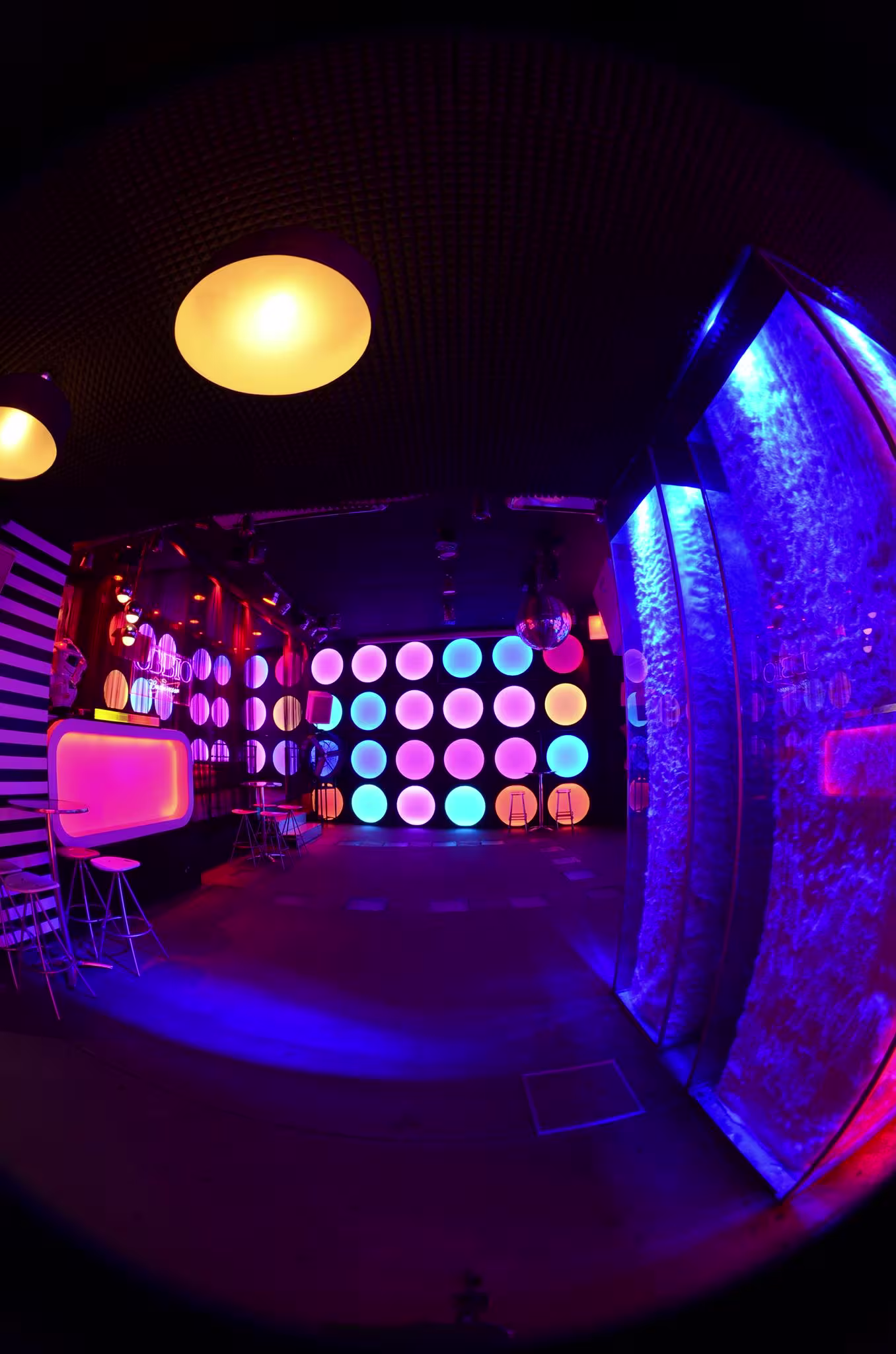 Interior futurista de Obbio con luces de neón, paredes de círculos luminosos y una atmósfera vibrante y colorida.