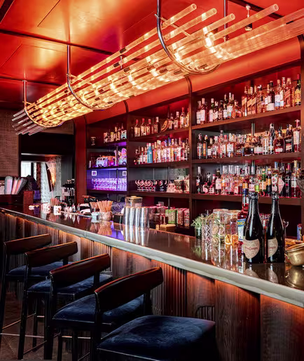 El interior del restaurante Lady Bongo con un ambiente cálido y acogedor. Hay una variedad de botellas en estantes iluminados detrás del mostrador, y varios vasos y artículos decorativos están dispuestos en la barra.