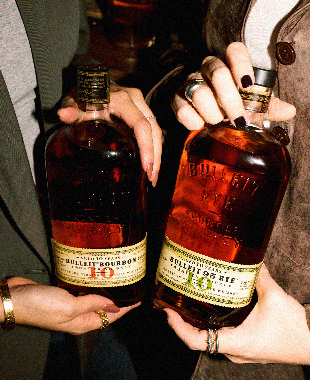 Two people holding bottles of Bulleit Bourbon 10 Year and Bulleit Rye whiskey