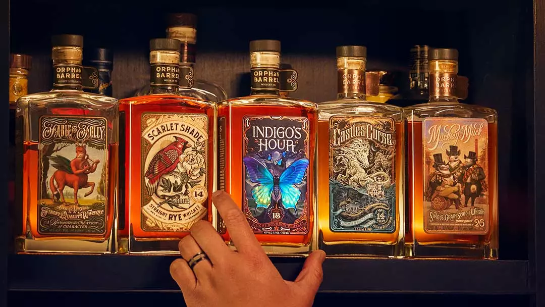 A hand reaches for one of five bottles of whiskey with ornate labels, displayed side by side on a shelf.