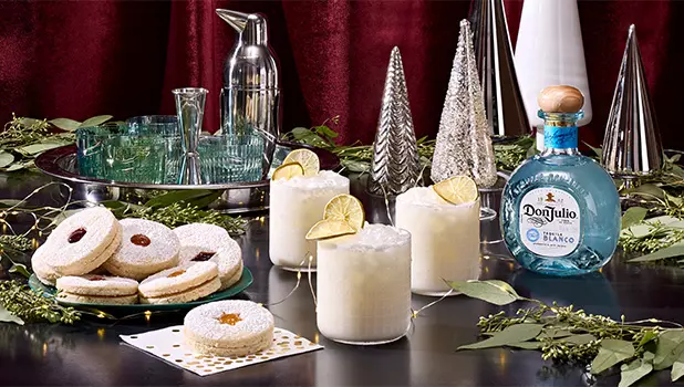 A festive table with lime cocktails, sandwich cookies, a bottle of Don Julio tequila, cocktail glasses, and silver holiday decorations.