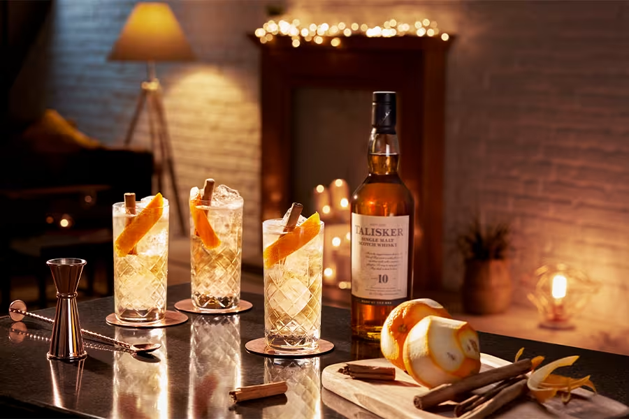 Three whisky highball glasses garnished with cinnamon sticks and orange peels