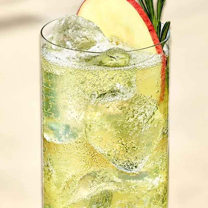 Cóctel highball con ginger ale, hielo, rodaja de manzana y romero