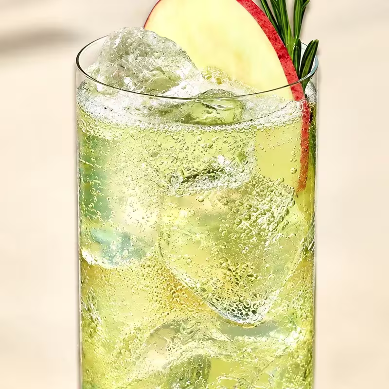 Cóctel highball con ginger ale, hielo, rodaja de manzana y romero