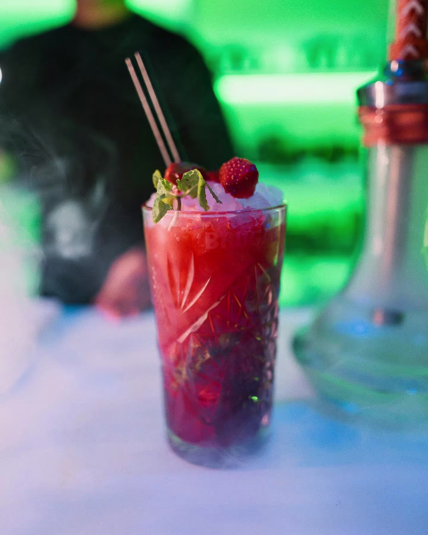 Cóctel rojo en Baloo con frutos rojos, menta y hielo picado. Ambiente vibrante y moderno con iluminación verde.