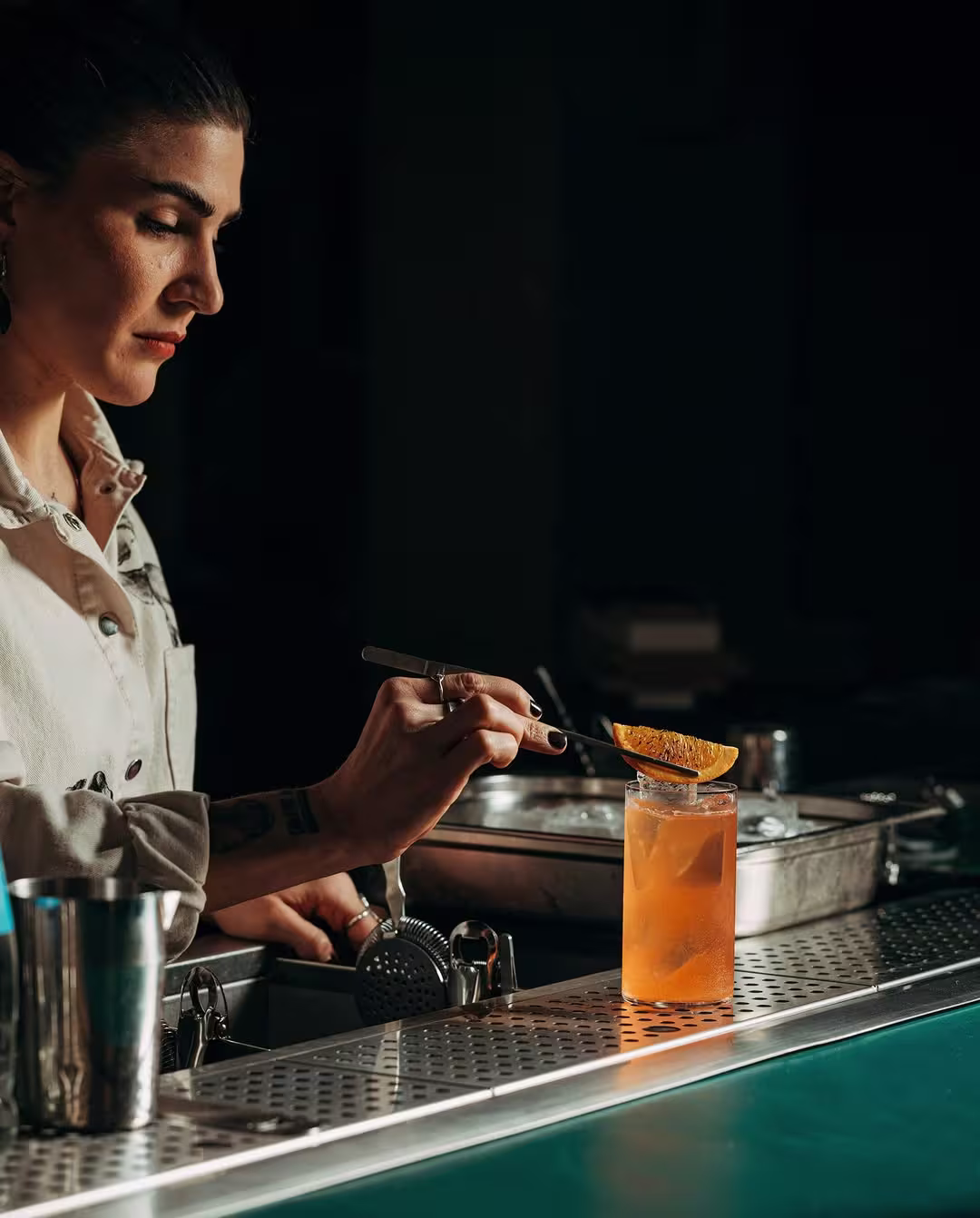 Bartender preparando un cóctel en una barra minimalista, con botellas y utensilios a la vista, iluminada por una luz tenue que crea un ambiente acogedor.