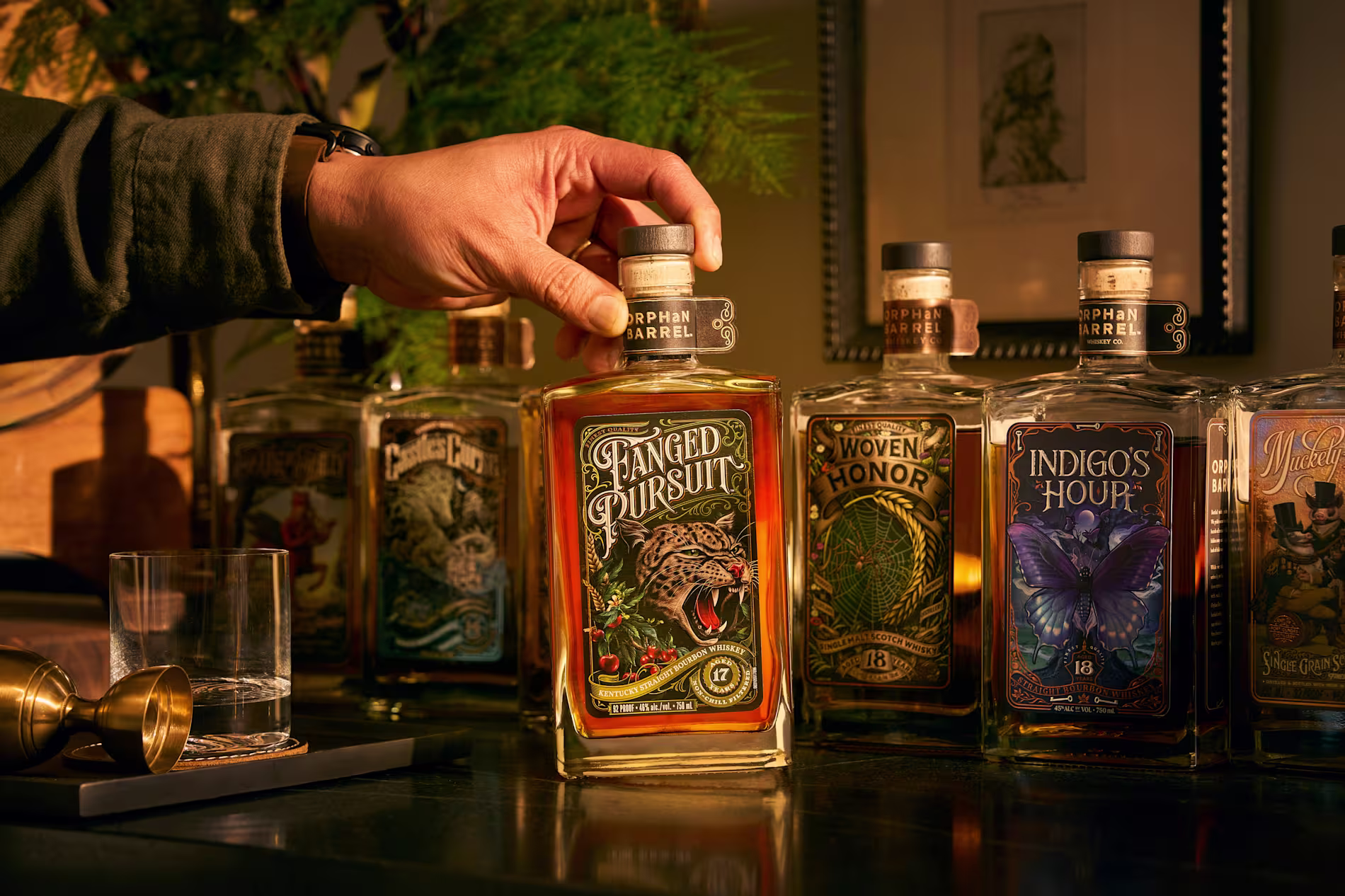 Lineup of Orphan Barrel whiskey bottles on a bar counter with warm amber lighting.