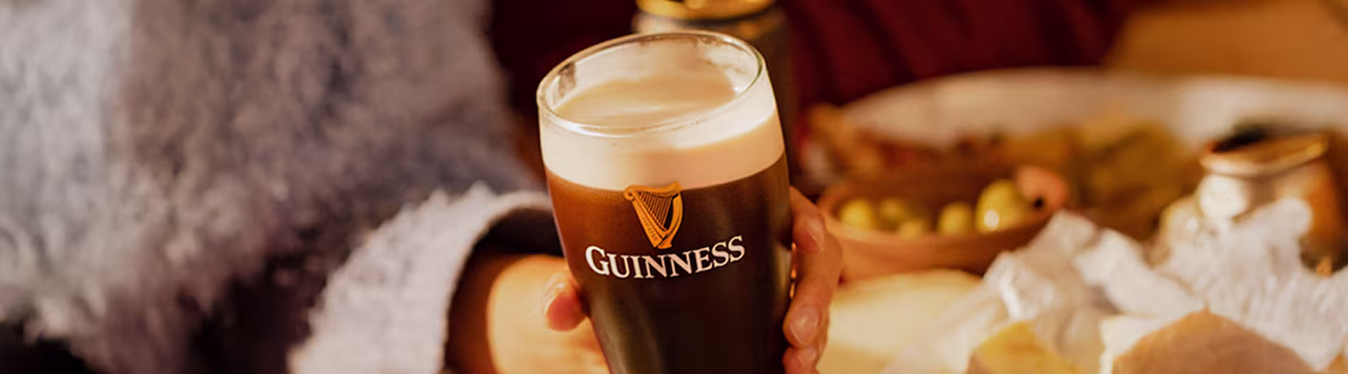 Primer plano de una pinta de cerveza negra Guinness en una acogedora mesa con queso y aceitunas.