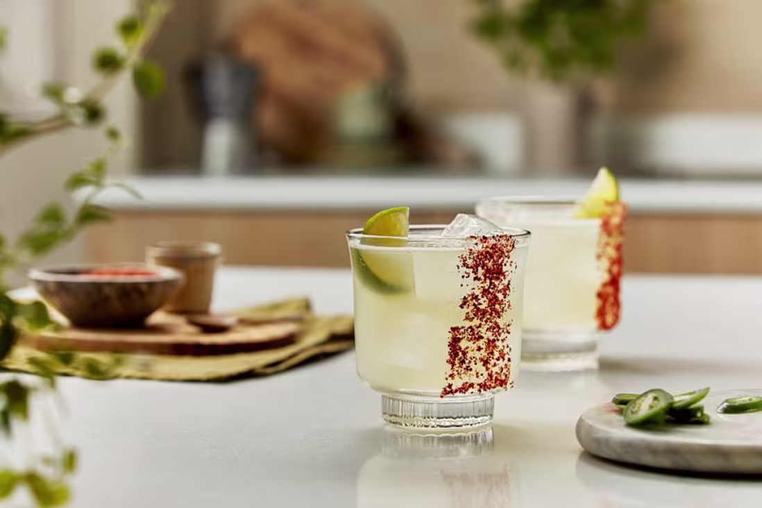 Tequila cocktails with lime wedges and chili salt rims served on a kitchen counter