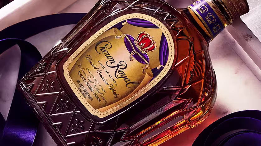 A bottle of Crown Royal Canadian whisky lies on its side, featuring a gold label and decorative purple accents.
