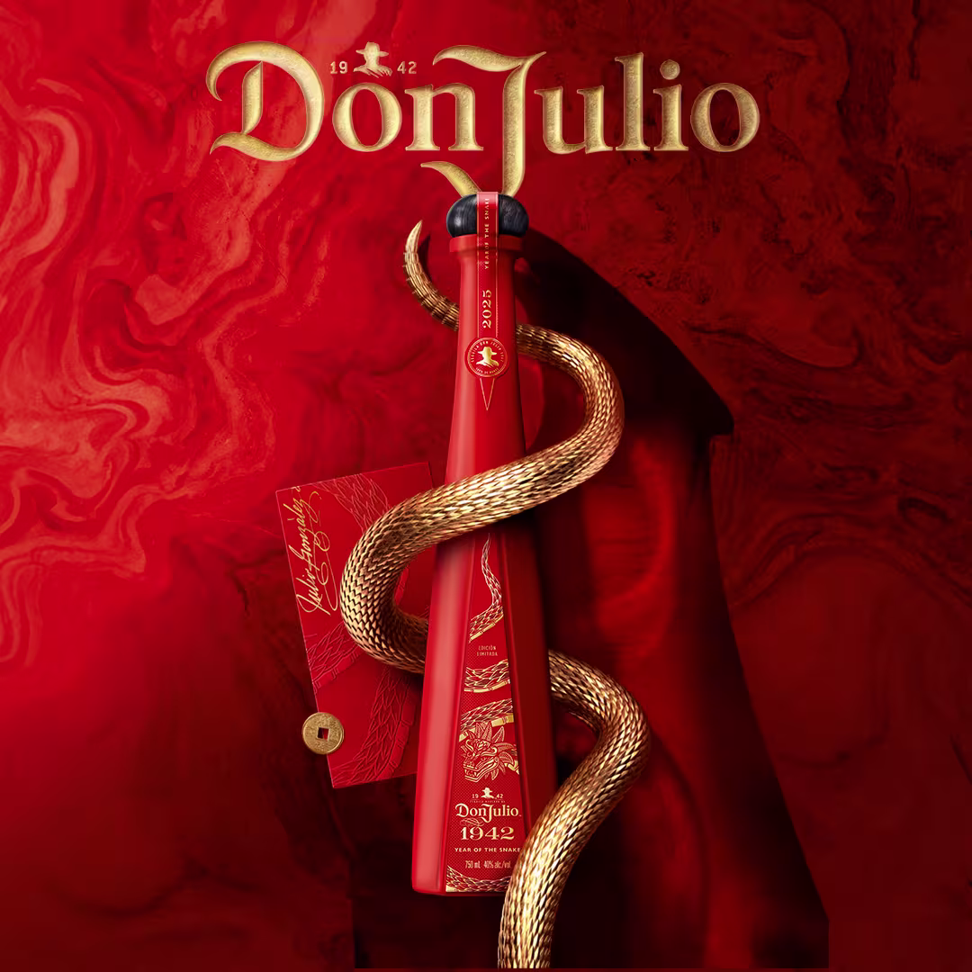 A red Don Julio 1942 tequila bottle is wrapped by a golden snake, with a red box beside it, set against a swirling red background with gold Don Julio branding at the top.