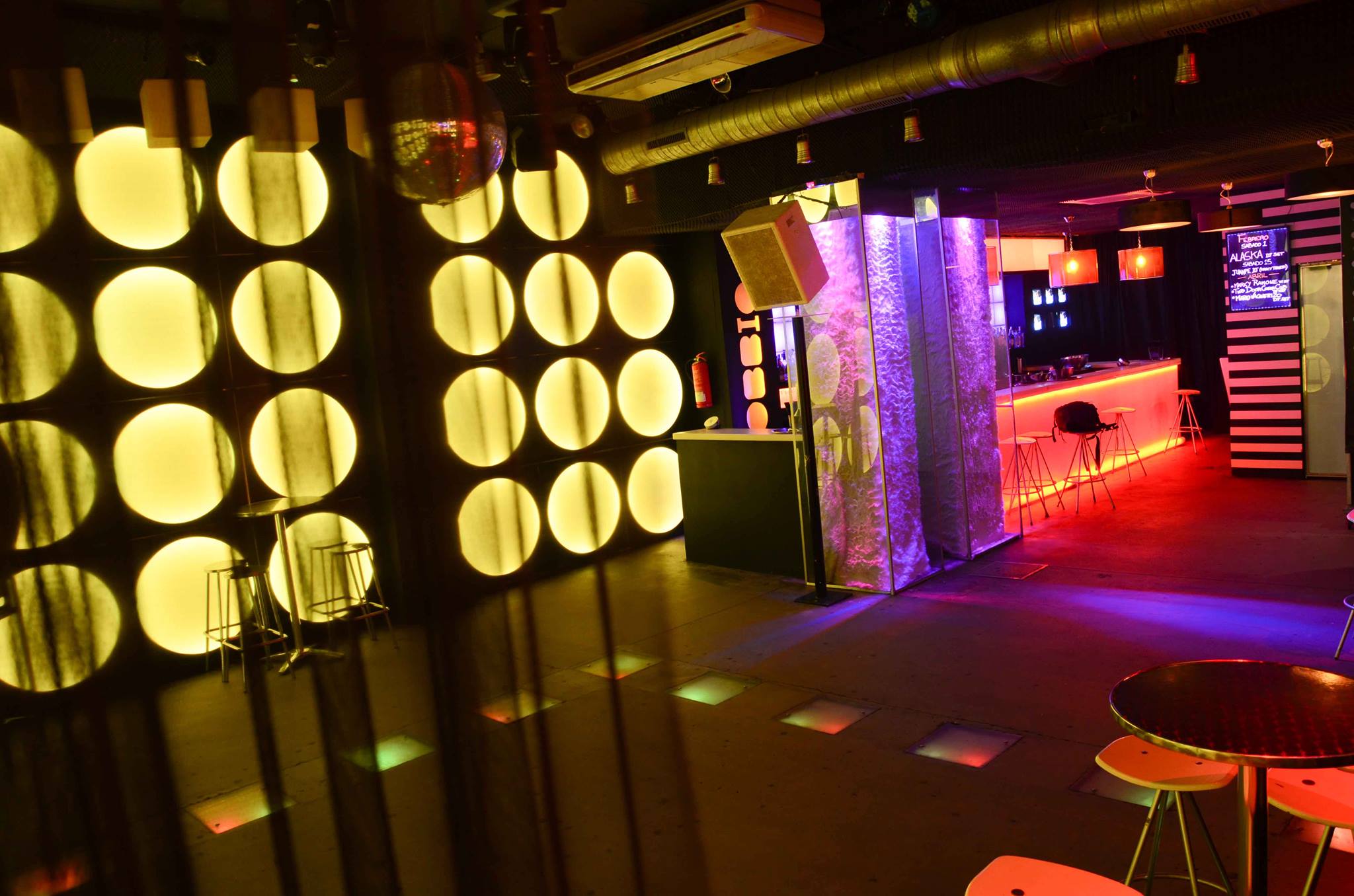 Obbio es un espacio moderno y vibrante con iluminación amarilla y neón, ideal para disfrutar de música y noches inolvidables en un ambiente único.