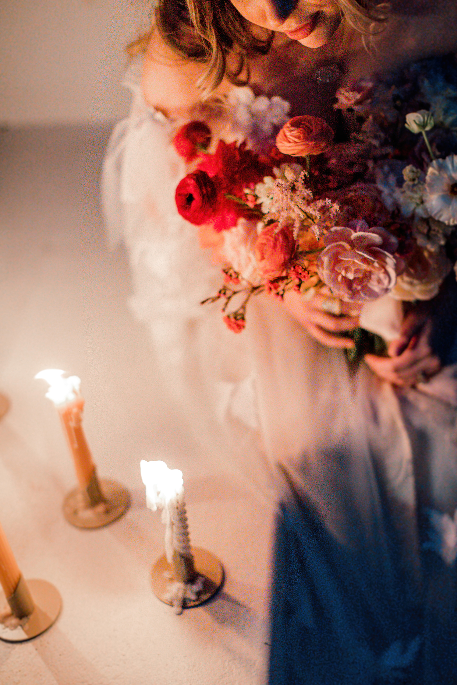 Deep red and blush blooms in a bouquet beside candlelight
