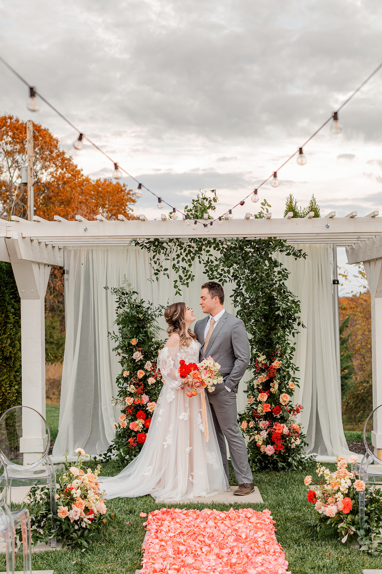 Couple at a pergola ceremony framed by floral columns and a coral petal aisle