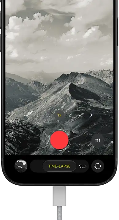 iPhone 18 Pro, front exterior, displaying a mountainous landscape, with the camera mode overlay in Time-Lapse mode, with power cable attached to charging port