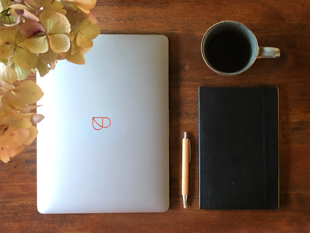 Laptop with Billie-Logo, pen, notebook and coffee on table with plant