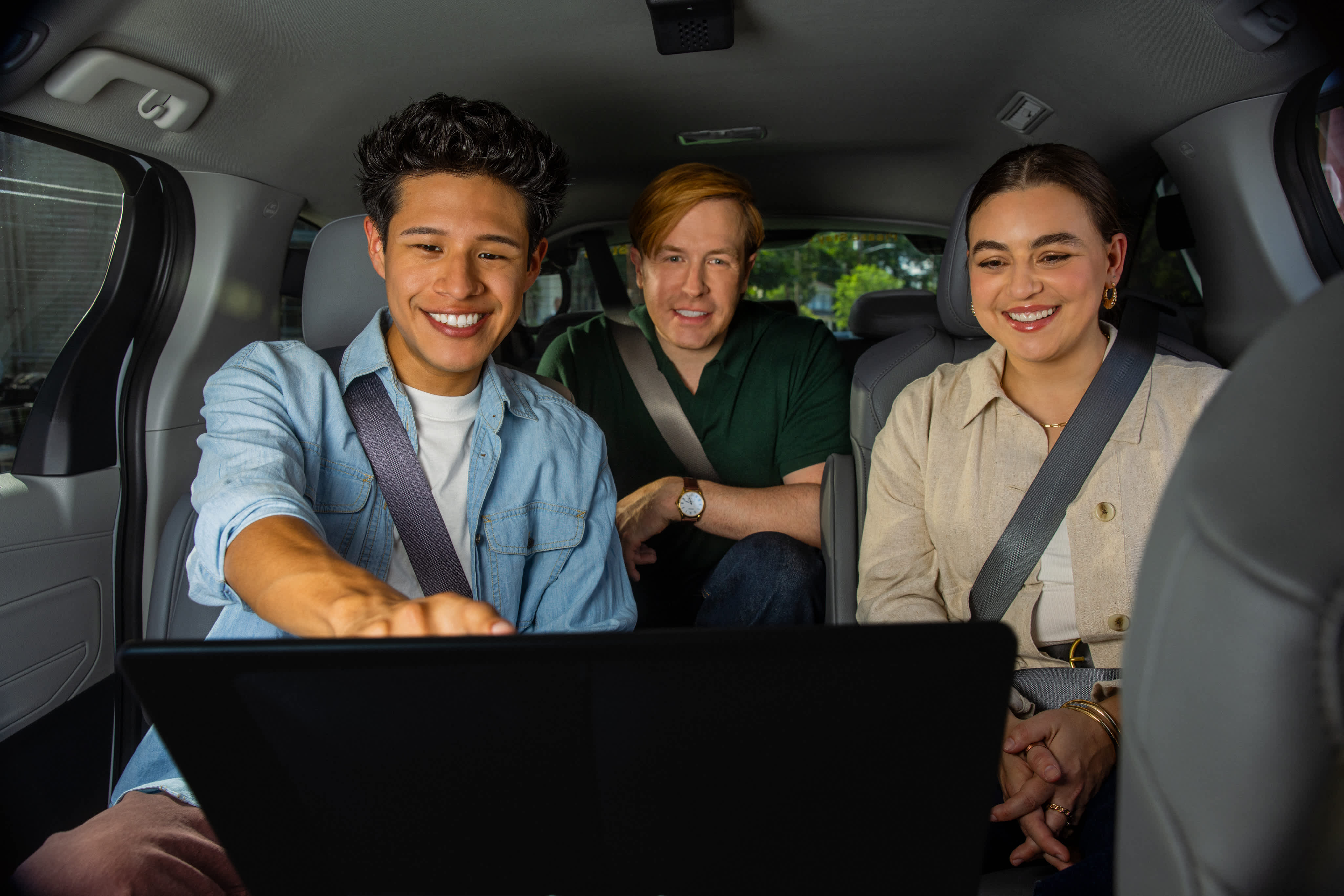 Three smiling passengers in Lyft May Mobility minivan looking at a tablet screen, all wearing seatbelts.
