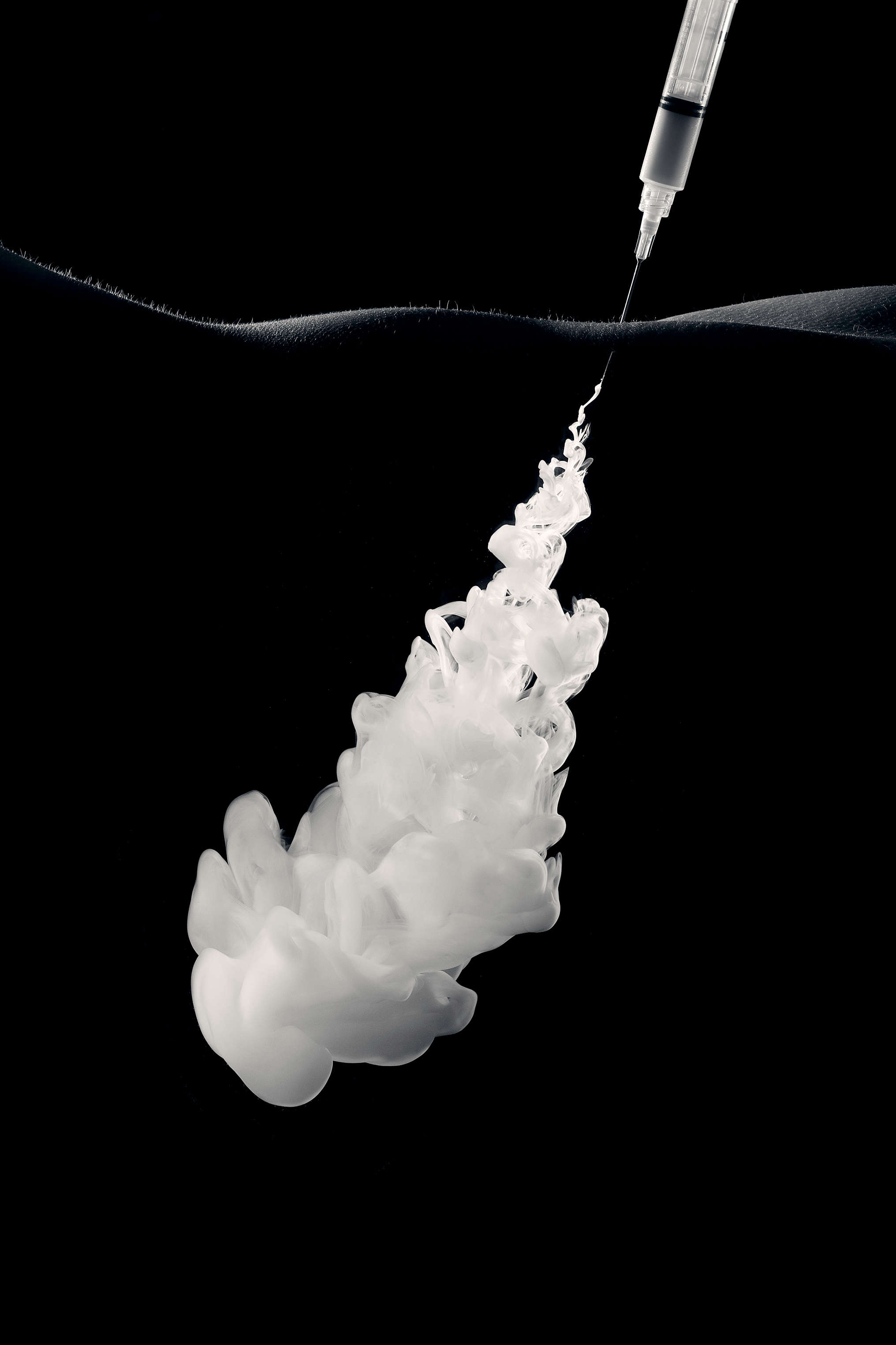 A syringe shooting white liquid into black water.