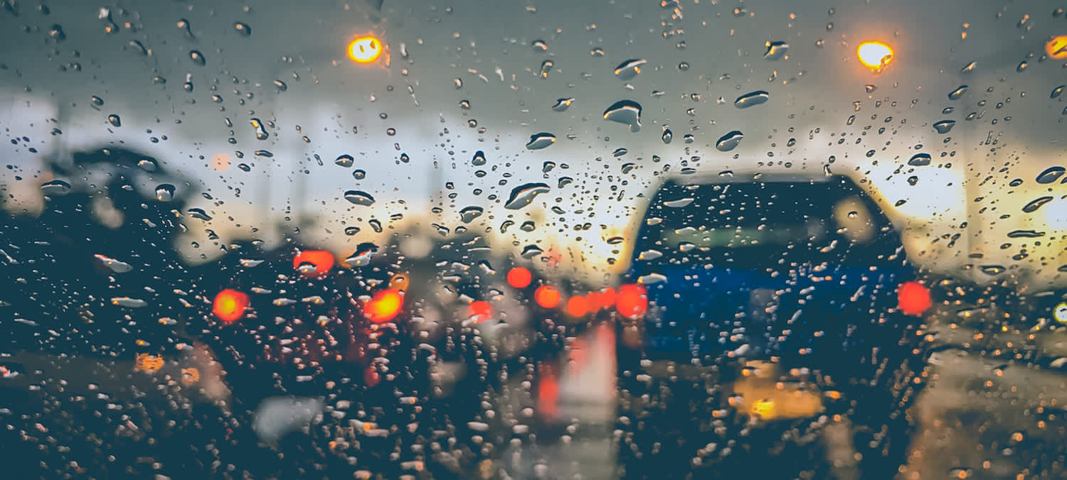 A car sitting in traffic with raindrops on the windshield.