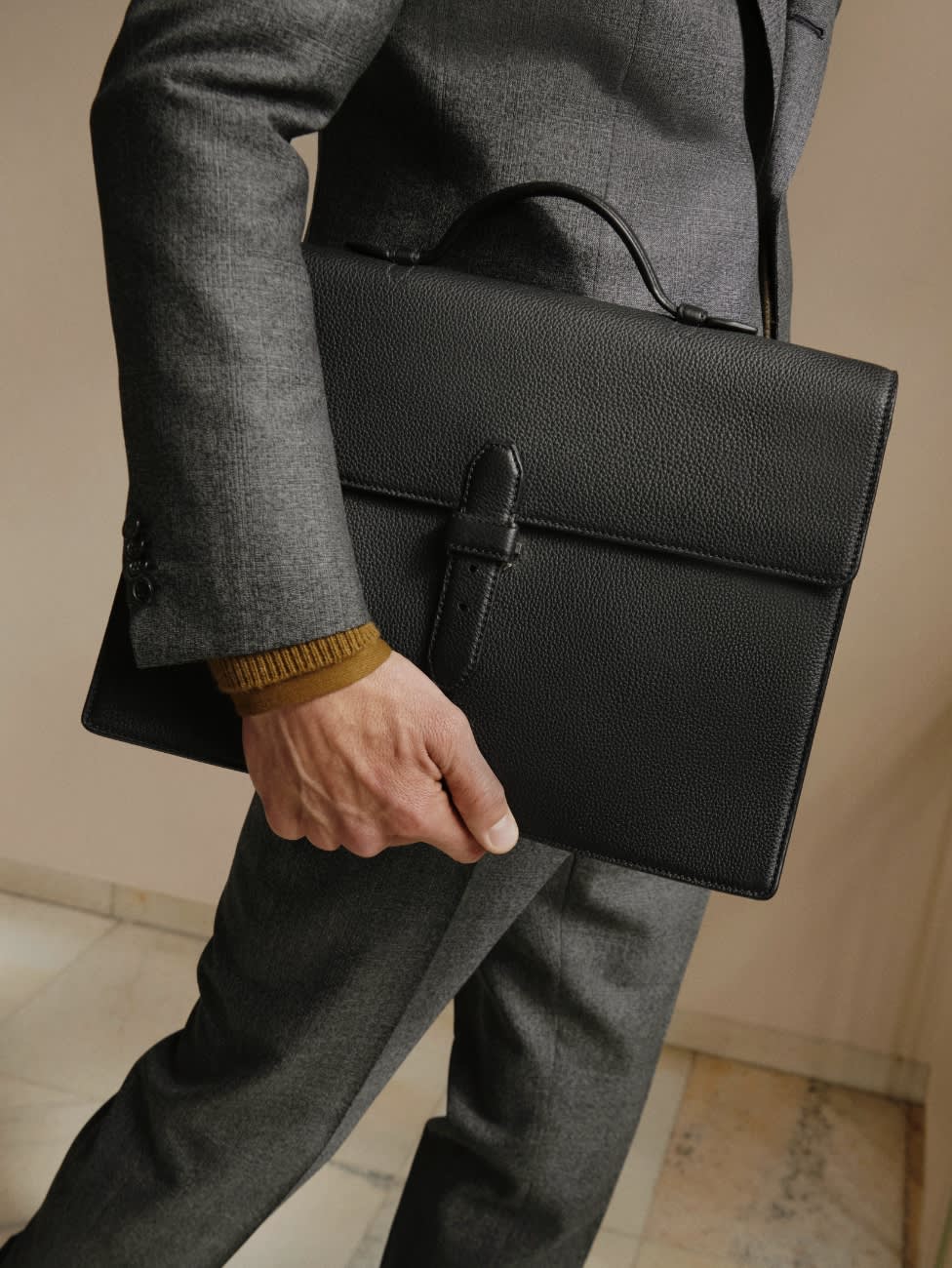 Male model wearing a dark grey suit and leather bag