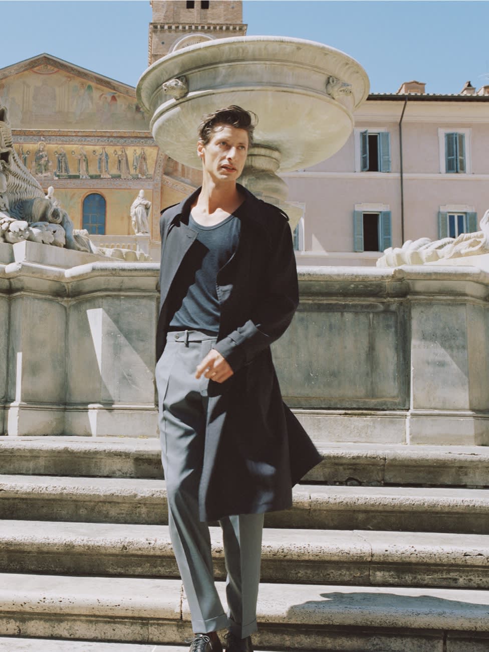 Male model wearing a dark blue trench coat and grey wool trousers