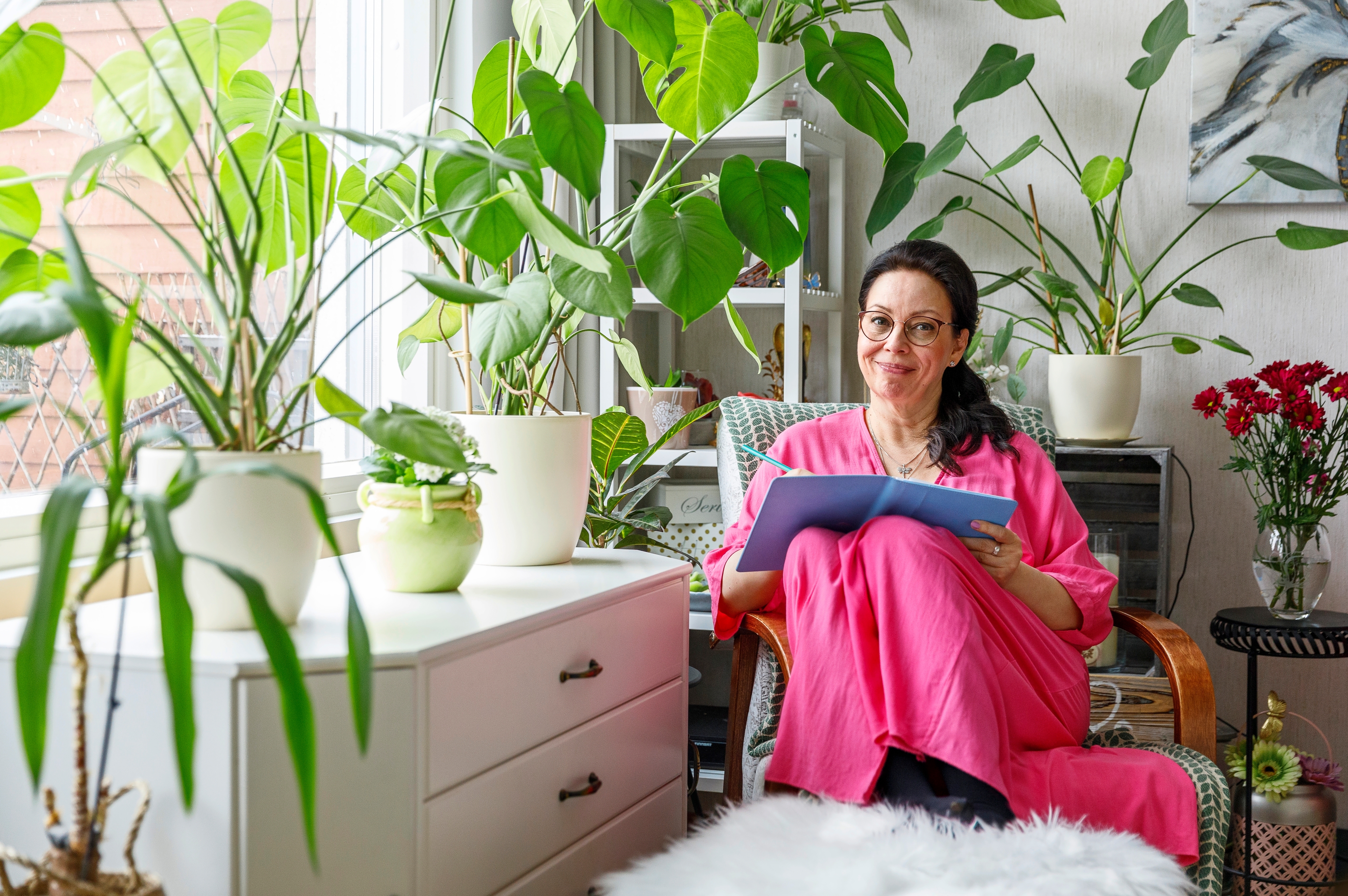 nainen istuu nojatuolissa huonekasvien katveessa