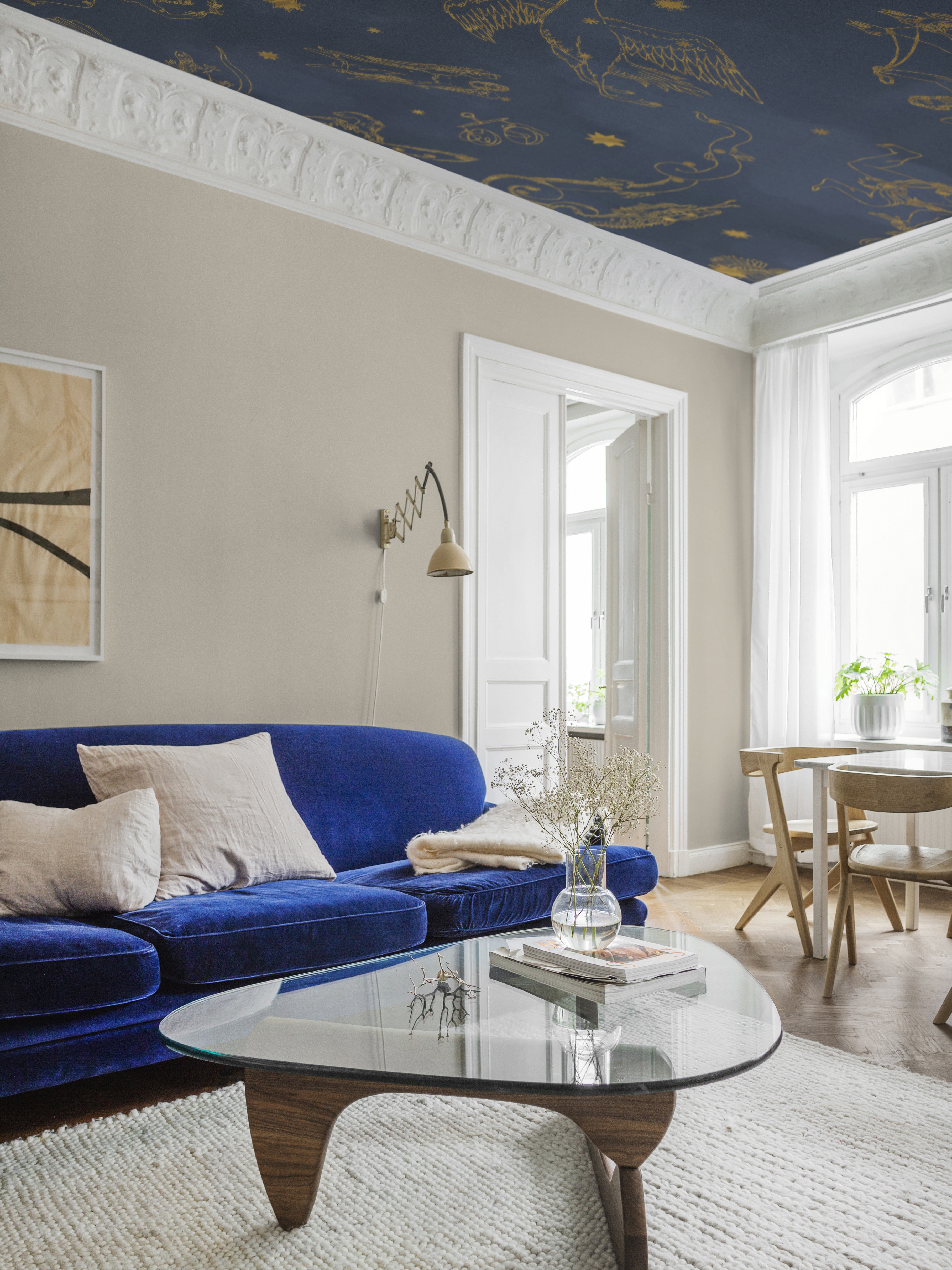 vanhan tyylinen sininen kattotapetti, beige seinä, sininen sohva, valkoinen matto, sohvapöytä ja pöytäryhmä