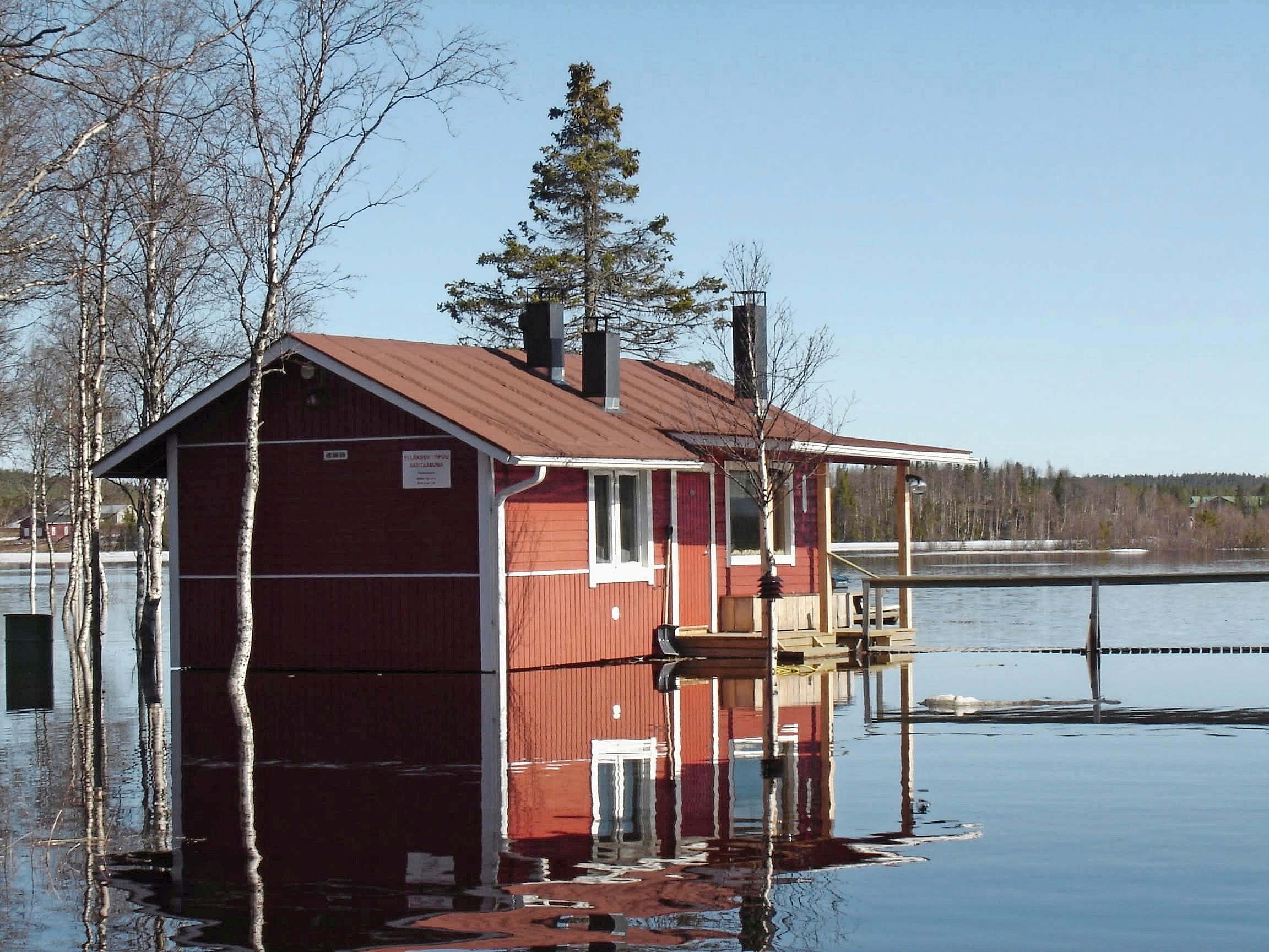Vesa Kaulasen punainen rantasauna tulvaveden ympäröimänä, vastarannalla metsää