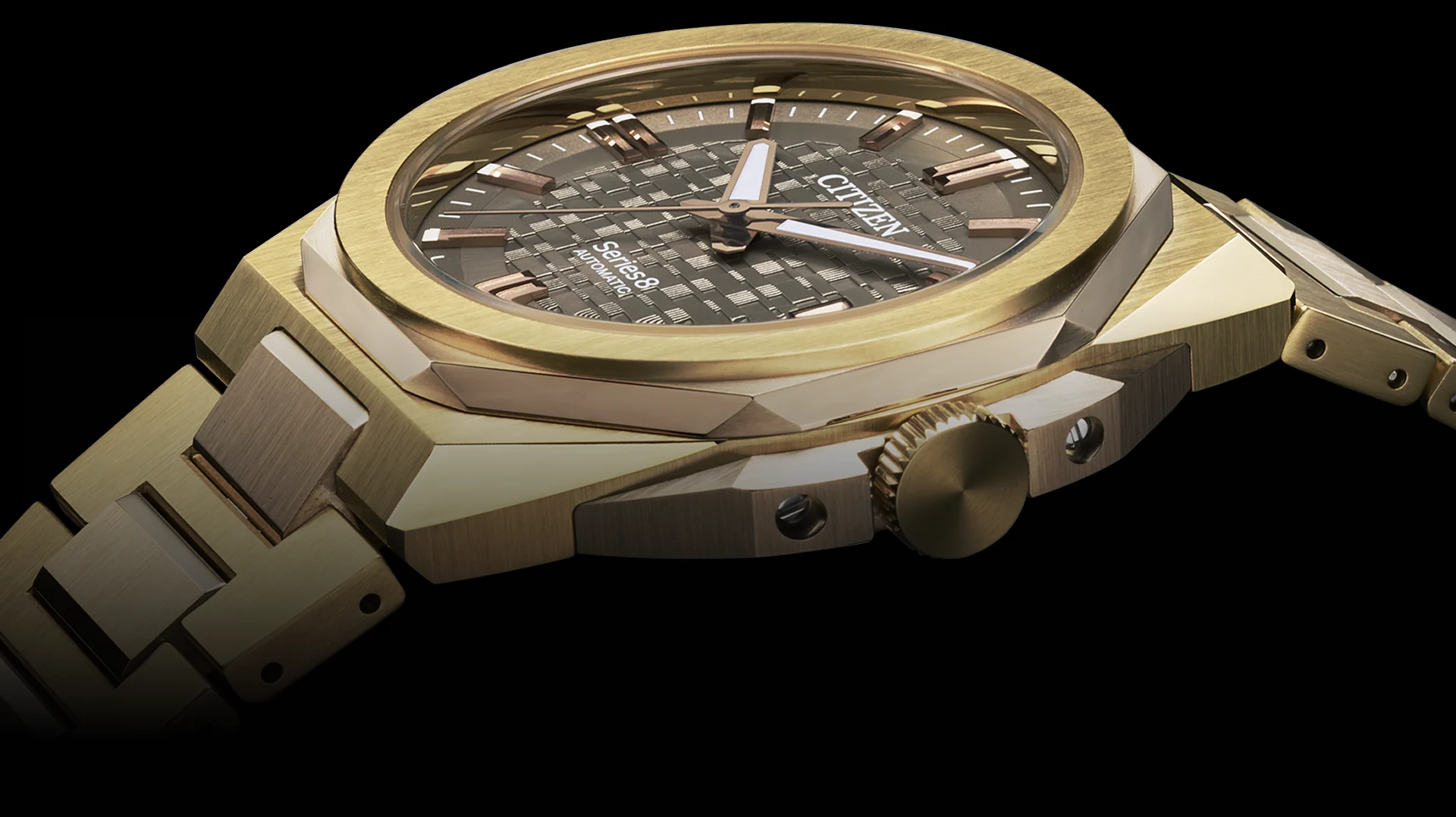A close-up of a gold Citizen wristwatch with a textured black dial, gold hour markers, and gold bracelet, viewed from a low angle against a black background.