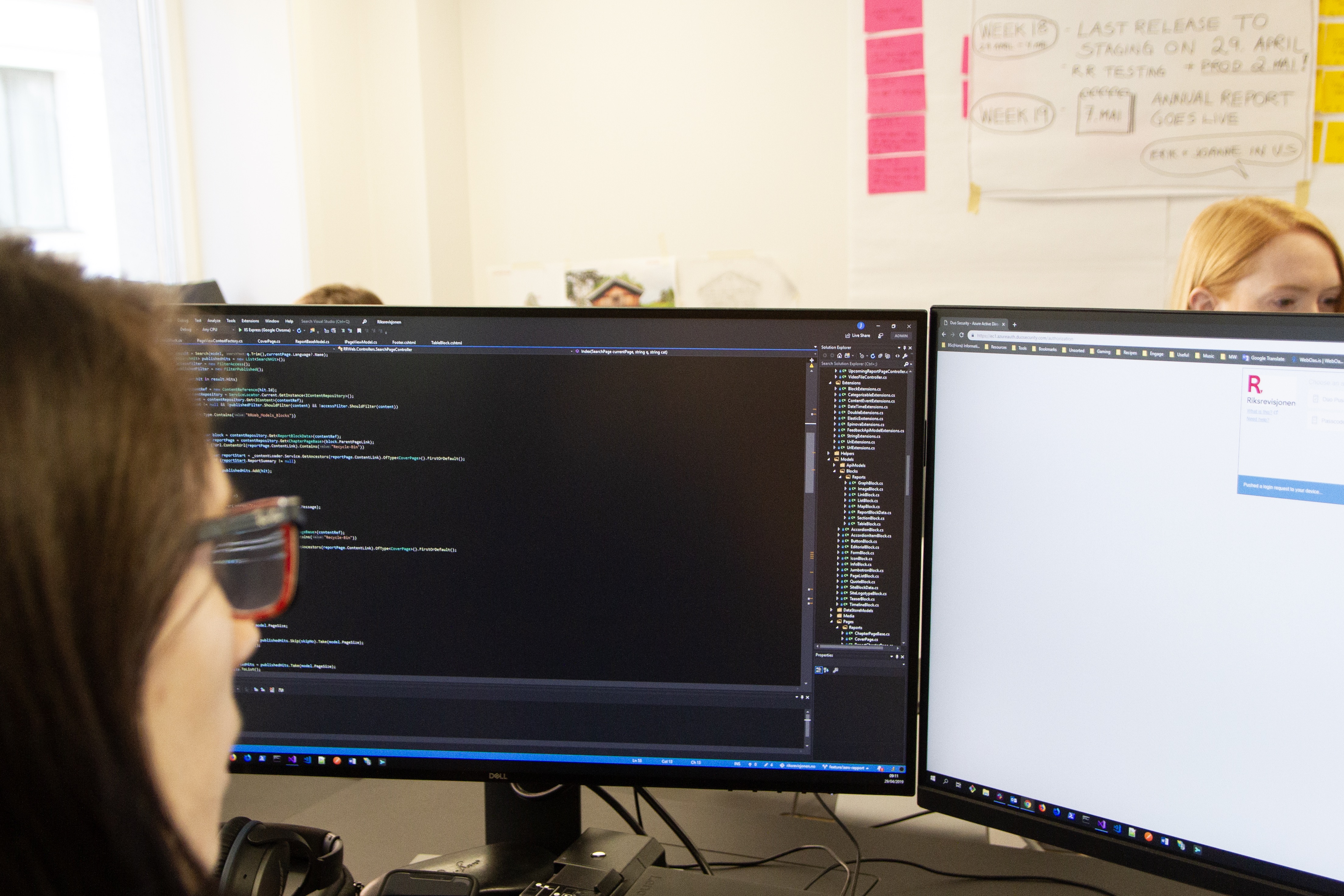 Woman with two computer screens in front of her, one of them has a programming software window open