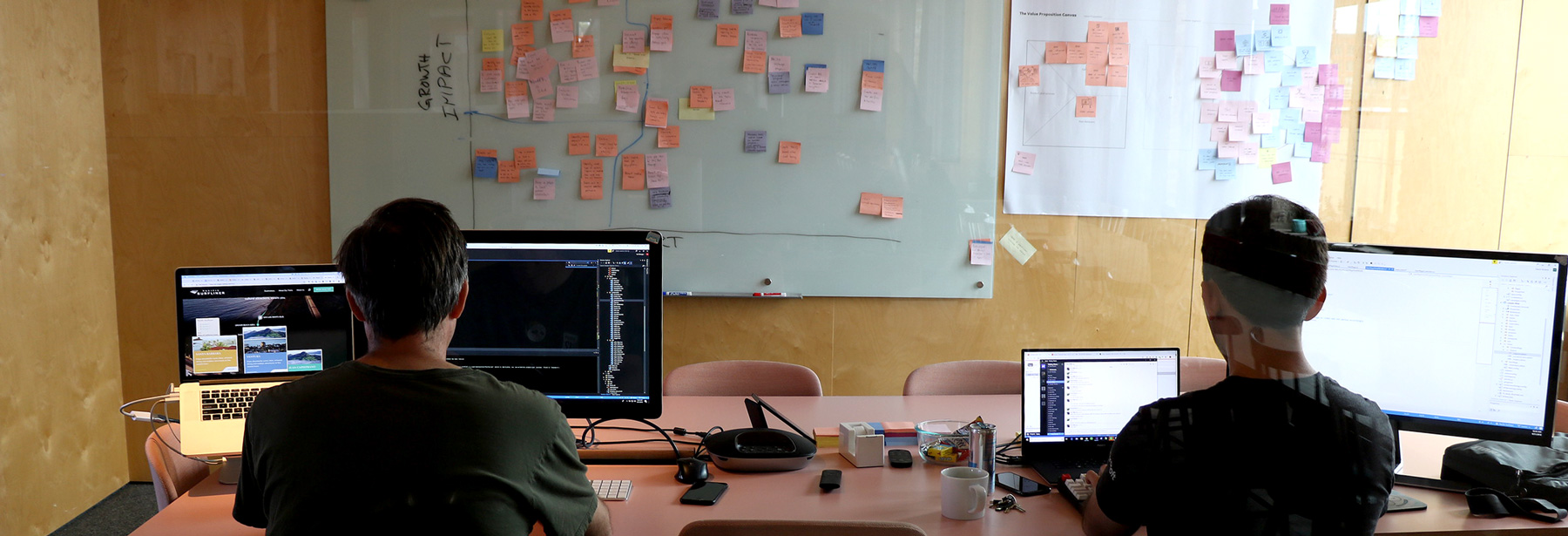 Two developers working in a conference room with post-it notes on the wall.