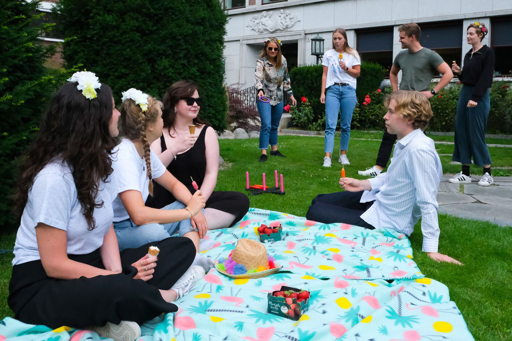 Group of young people sitting in the grass or playing games in front of an office building, playing games and laughing.