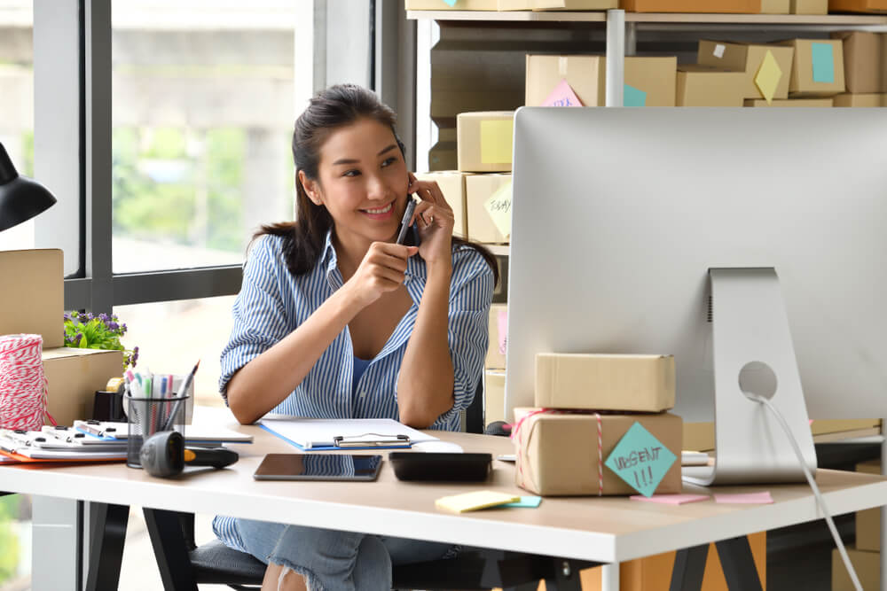 Young Asian business woman talking on the phone and working on her laptop