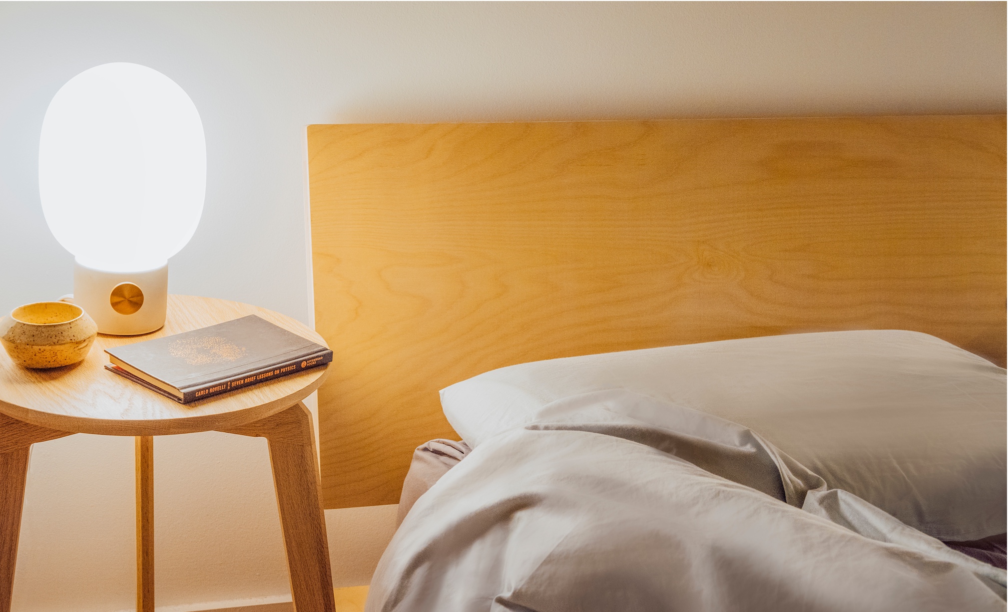 A Floyd bed in birch beside a small nightstand with a glowing light.