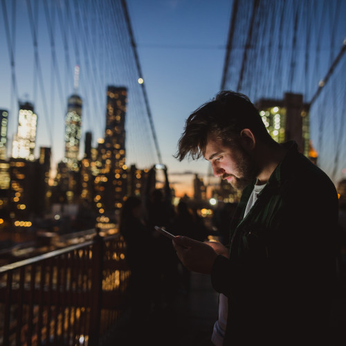晚上在布鲁克林大桥上看手机的男子.
