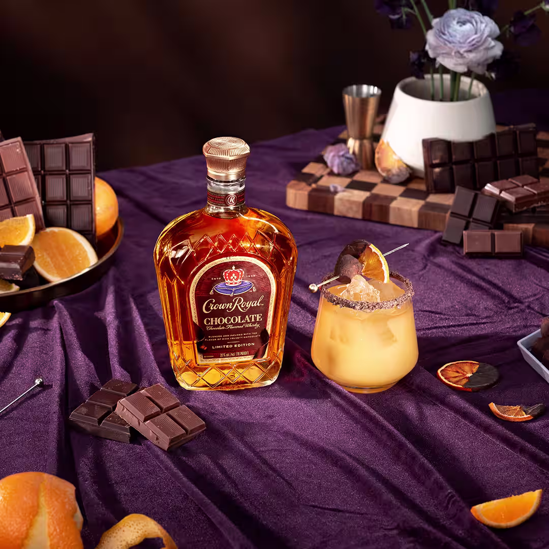 A bottle of Crown Royal Chocolate next to a whisky and orange juice cocktail garnished with a chocolate covered orange