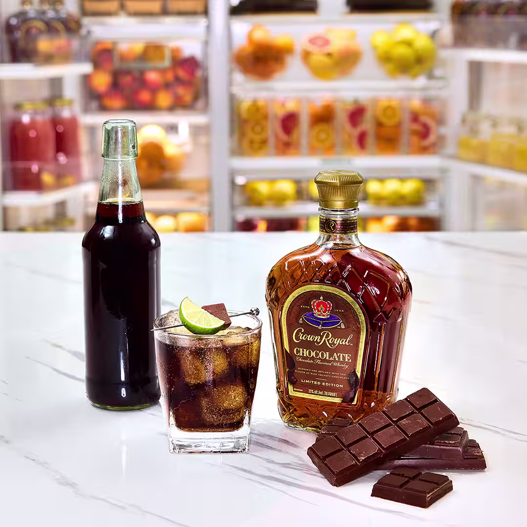 A bottle of Crown Royal Chocolate next to a whisky and cola drink garnished with a lime wheel