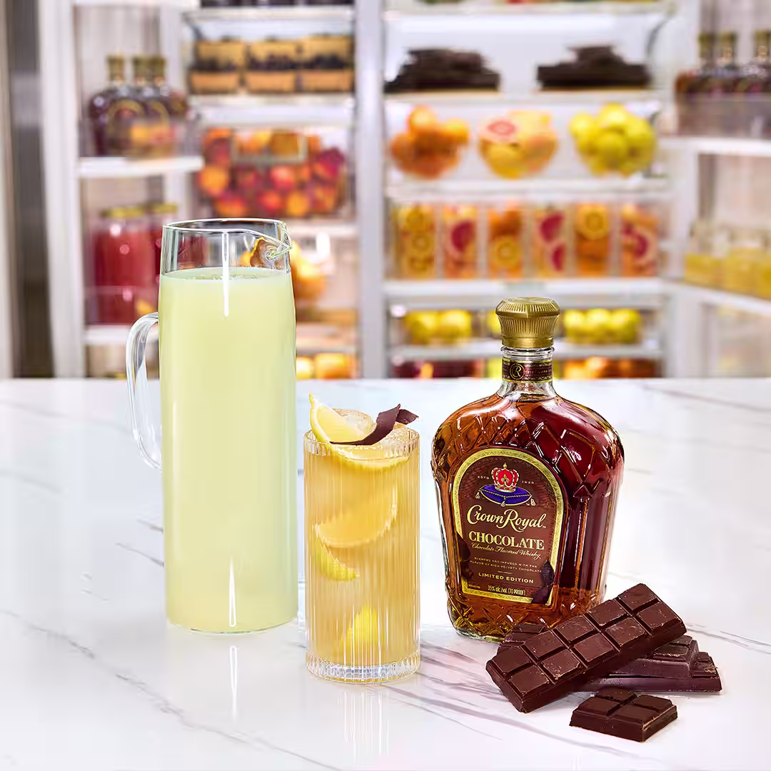 A bottle of Crown Royal Chocolate next to a whisky and lemonade cocktail garnished with chocolate shavings