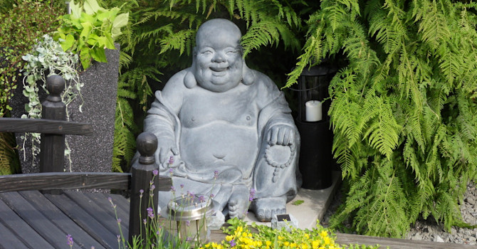 En glad och god Buddha mediterar i Lena Karlssons trädgård.