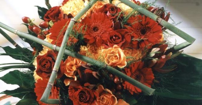 "Amore" heter den här ljuvliga buketten, uppkallad efter den mörkt röda rosen som ingår. Den varmt persikofärgade rosen heter 'Jazz'. Här finns också nejlikor, gerbera, fröhus av hyperikum och flera sorters grönt. Stråna som flätats över buketten kallas "snakegrass". Arrangemang: Florist Mikael Olson. Foto: Tommy Durath.