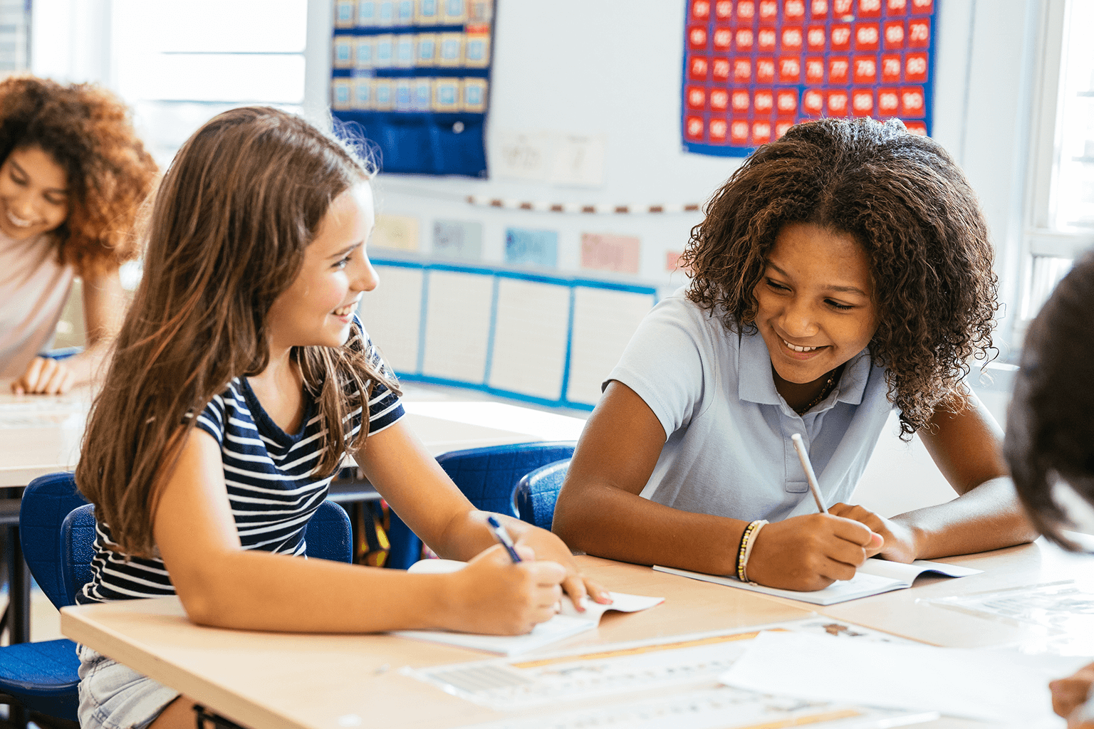 Students working together at a desk in a classroom. Students working together at a desk in a classroom.