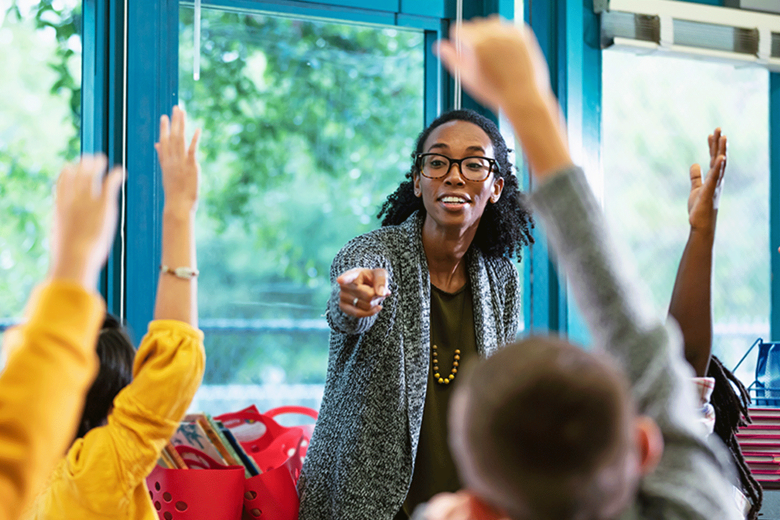Students raising their hands in a classroom with a teacher calling on them. Students raising their hands in a classroom with a teacher calling on them.