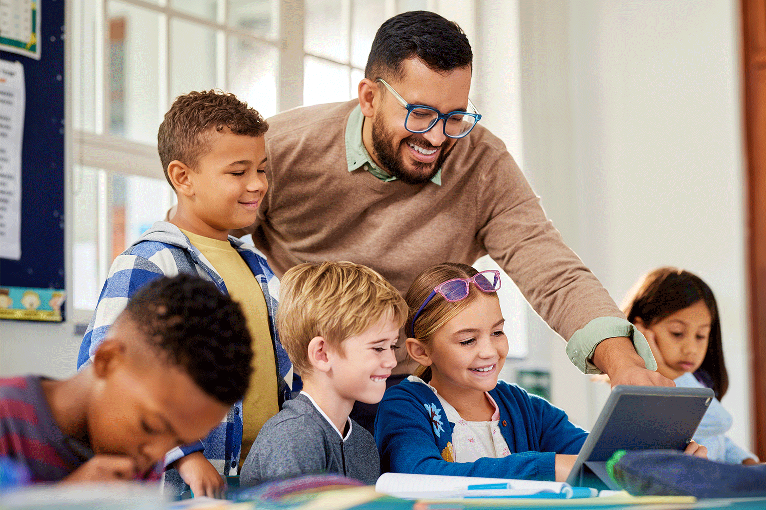 Students and their teacher are working together on a tablet. Students and their teacher are working together on a tablet.