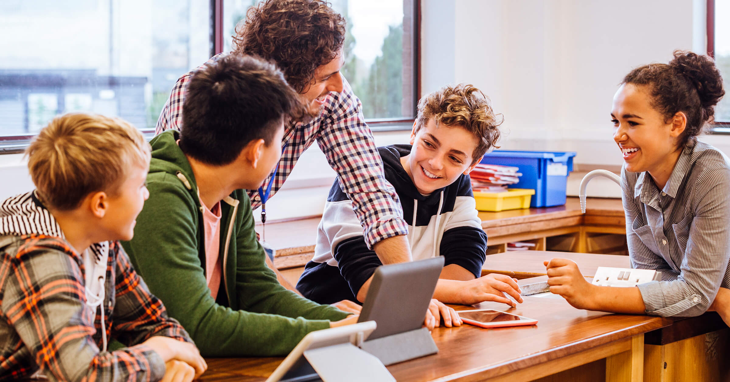 A teacher and students are gathered around a table, talking. A teacher and students are gathered around a table, talking.