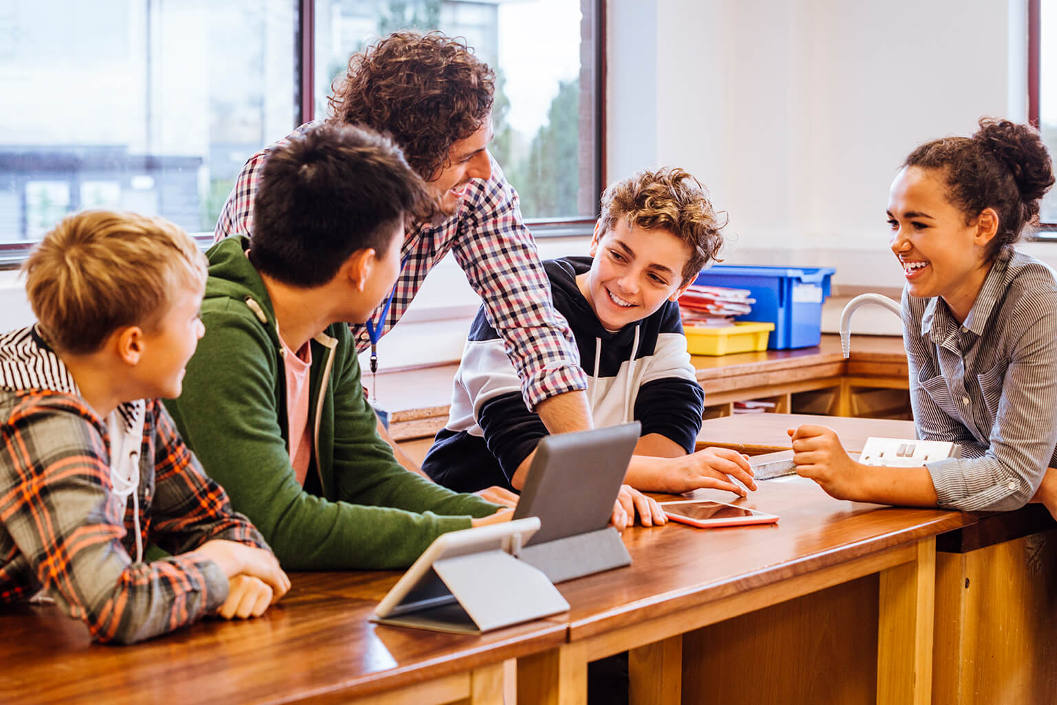 A teacher and students are gathered around a table, talking. A teacher and students are gathered around a table, talking.