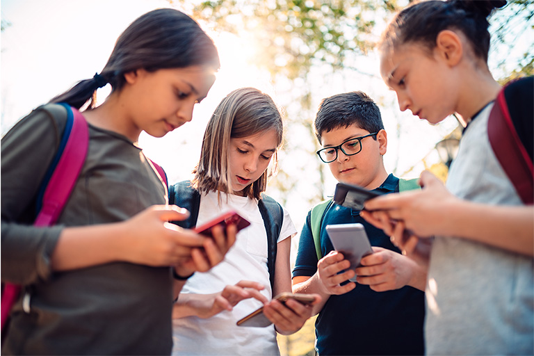 Kids are standing in a circle looking at their cell phones. Kids are standing in a circle looking at their cell phones.