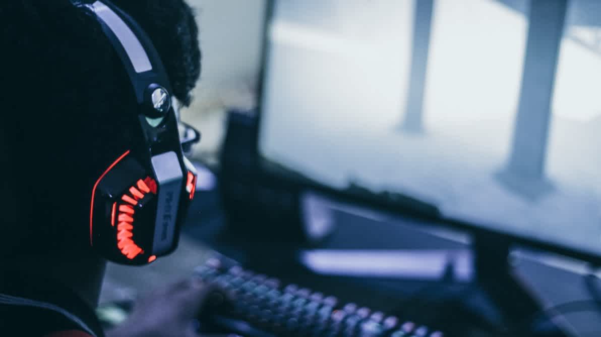 Gutt med hodetelefoner gamer forran en PC skjerm