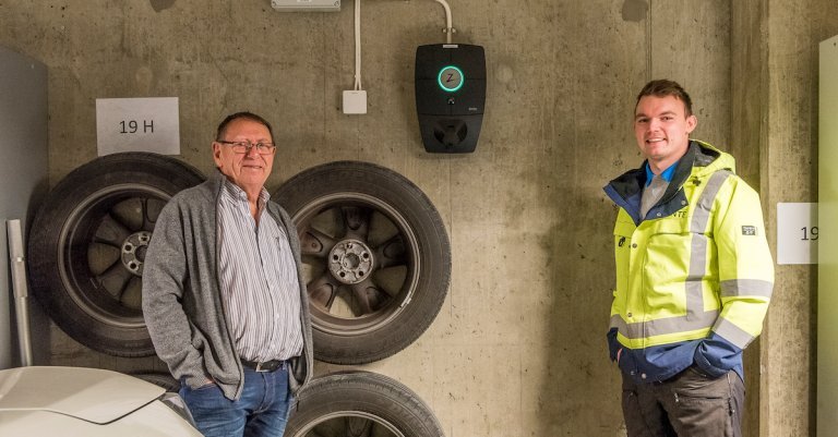 Bilde av to menn som står foran en montert elbillader