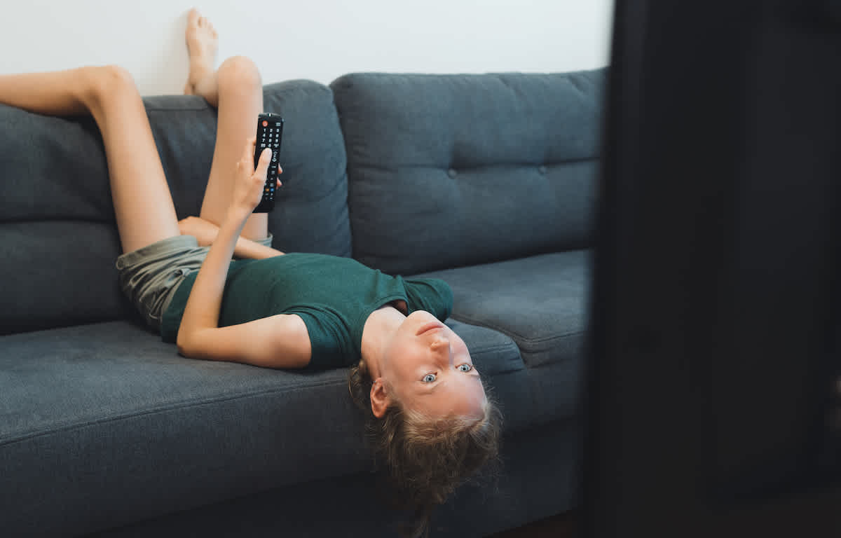 Jente ligger oppned i sofaen og ser pÄ tv