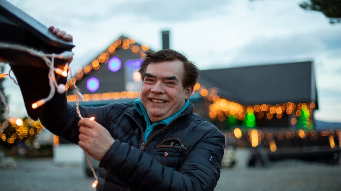 Mann smiler mens han står foran et hus med mye julebelysning